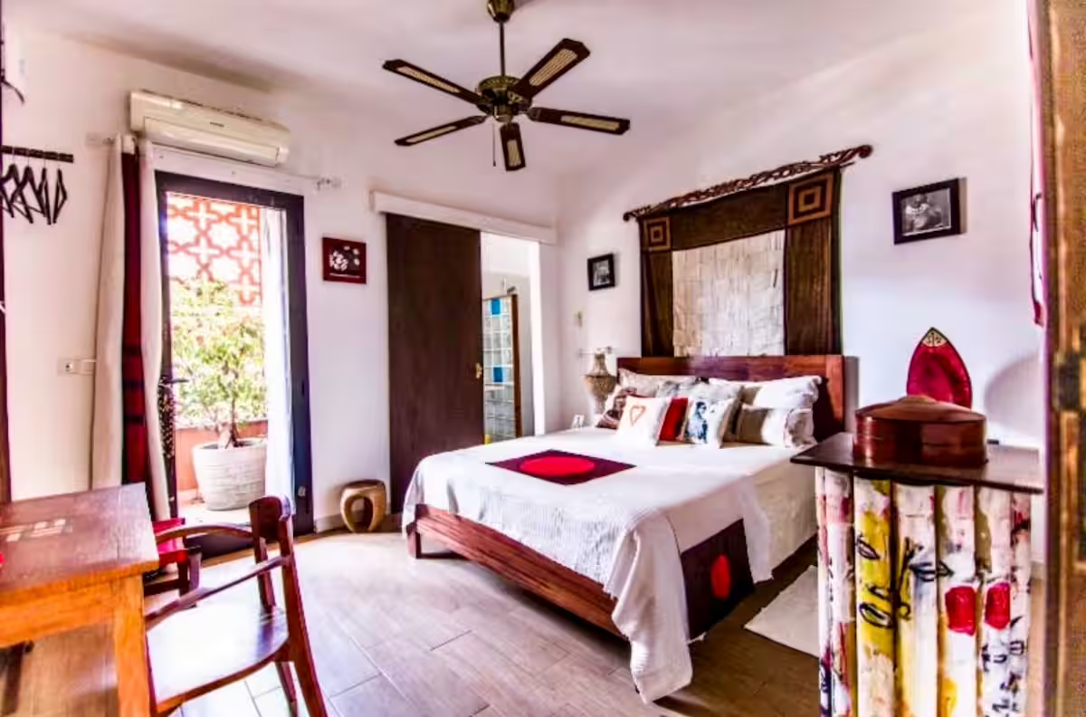 Cauris room — queen bed with red accents and a sunlit balcony view