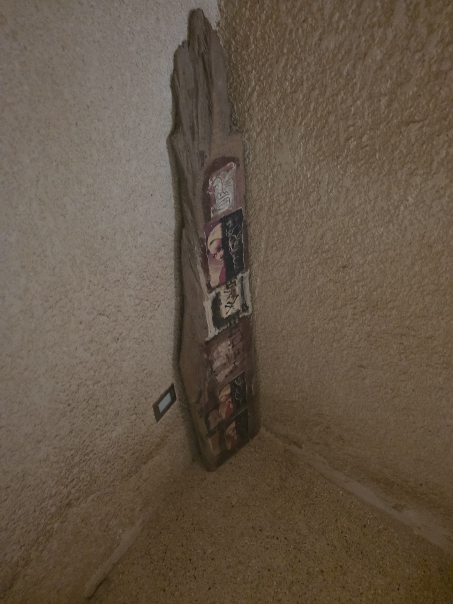 Haute forme irrégulière en bois avec des fragments imprimés de portraits superposés, appuyée dans un angle texturé
