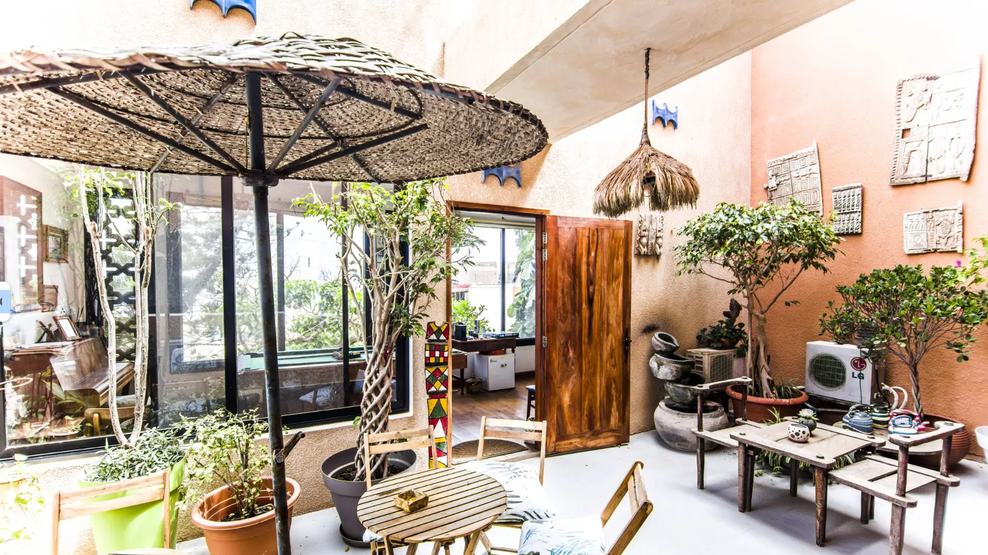 Shaded courtyard terrace with a woven parasol, potted trees, carved wall panels and wooden seating