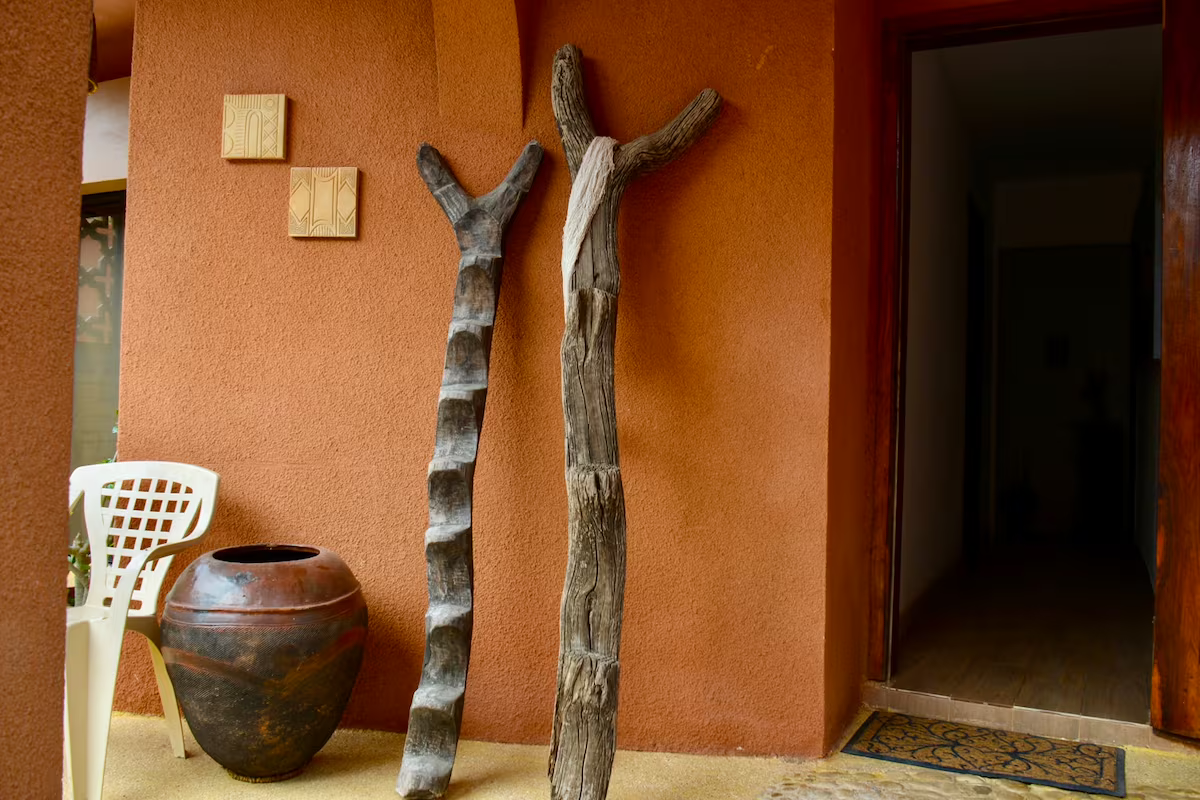 Entrance corner with carved driftwood sculptures and clay pot against a terracotta wall