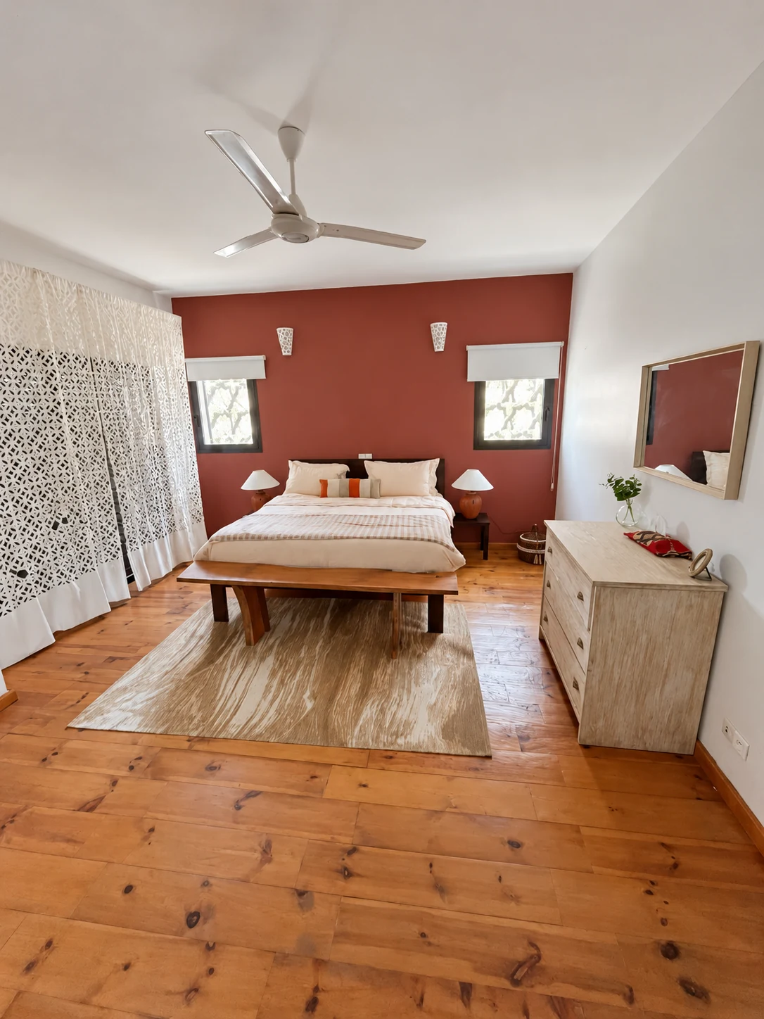 A bedroom with white linen, a terracotta wall and a wooden bench