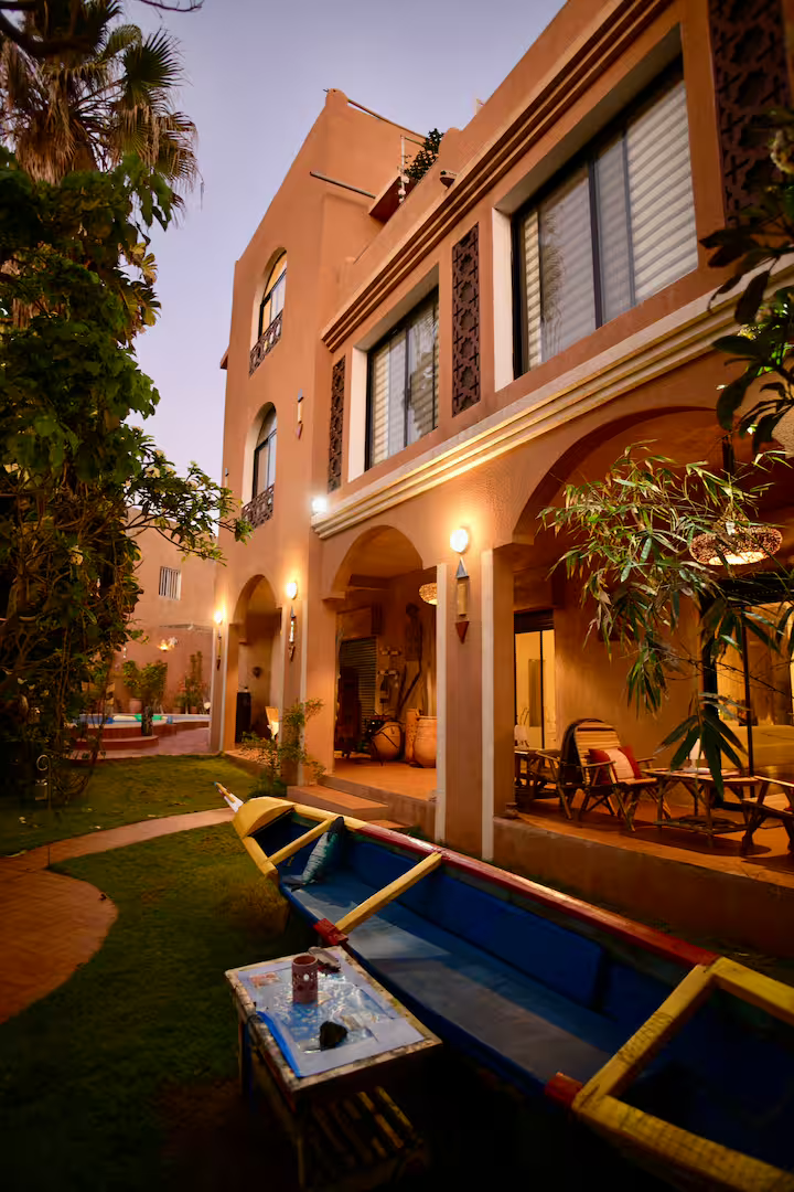 Garden at dusk with painted pirogue boat in front of the arched terracotta facade