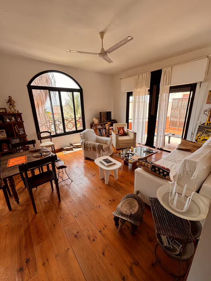 Living room with arched window, ceiling fan, wooden floors and African art