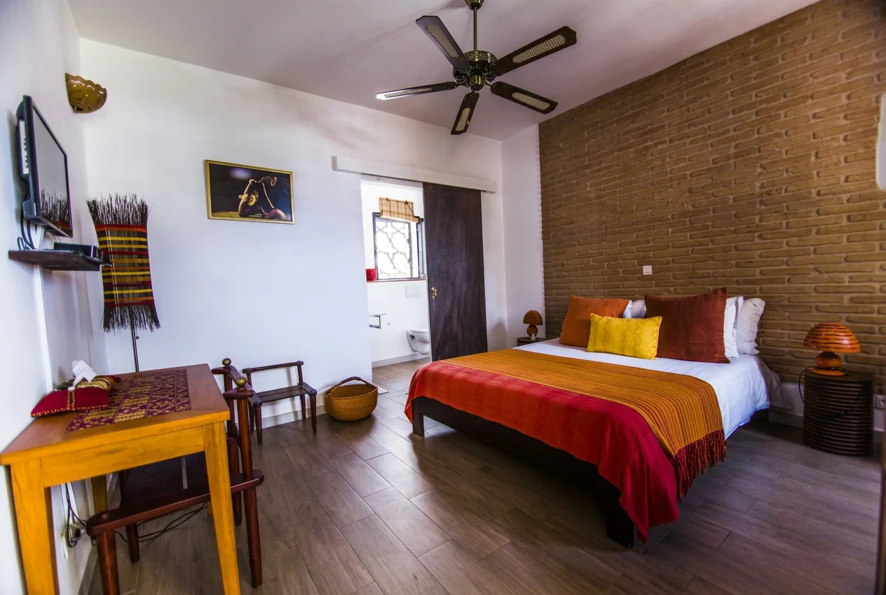 Bedroom with exposed brick wall, ochre bedding and ceiling fan