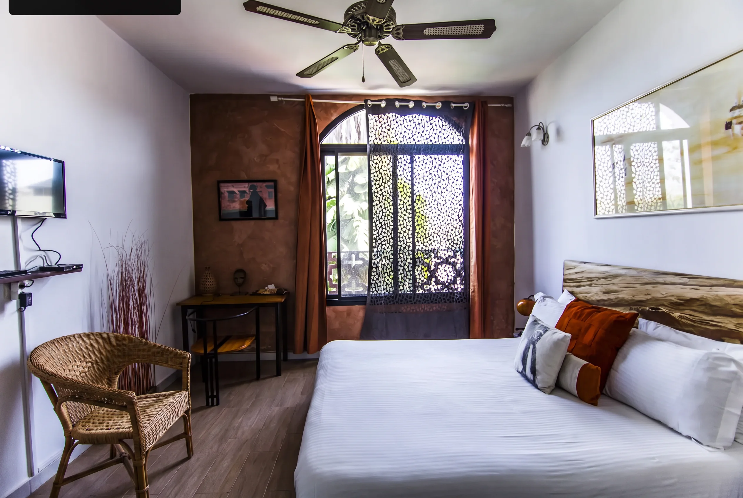 Bedroom with terracotta curtains, warm ochre bedding and wooden ceiling fan