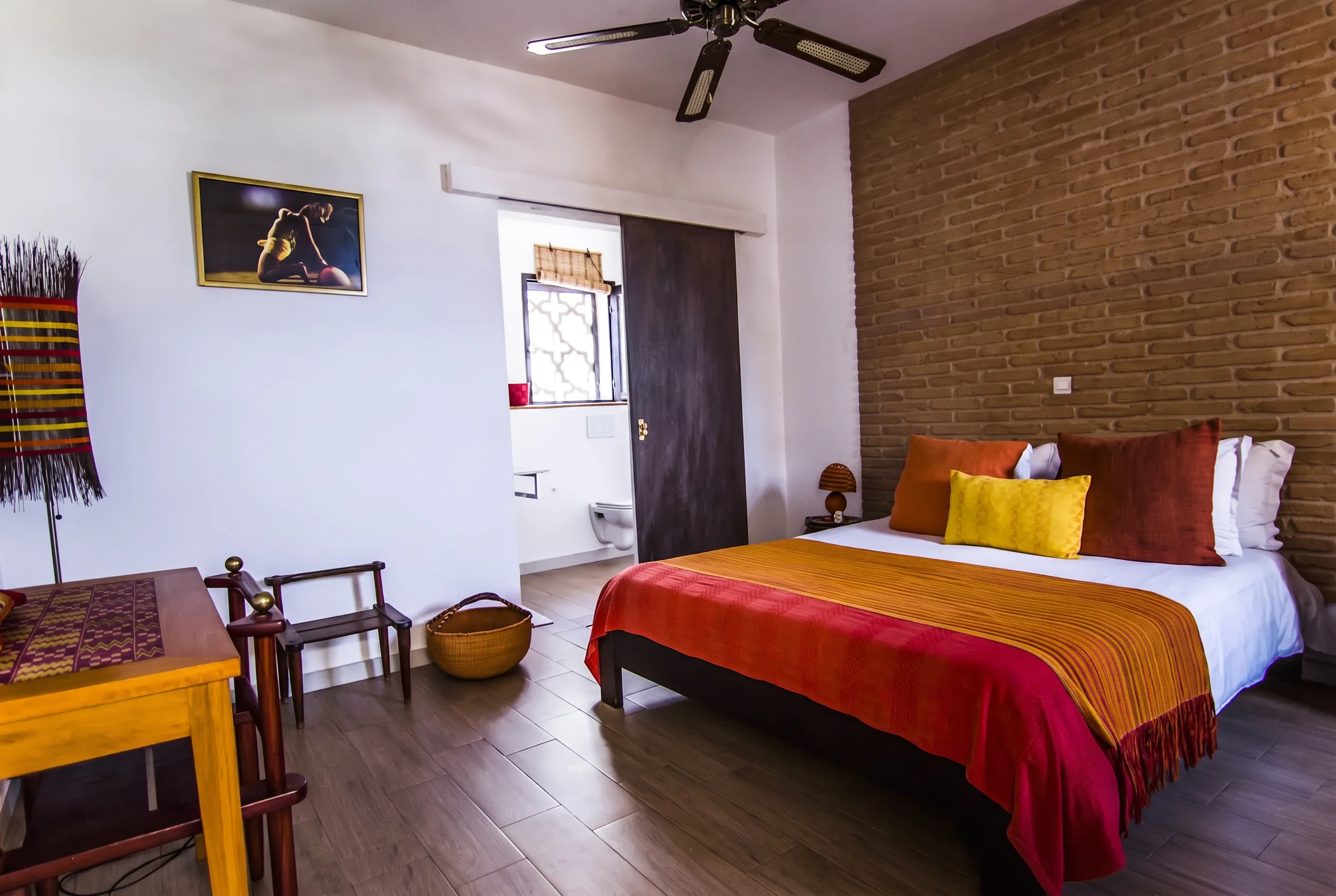 Calebasse room — king bed with warm terracotta and gold textiles, exposed brick wall