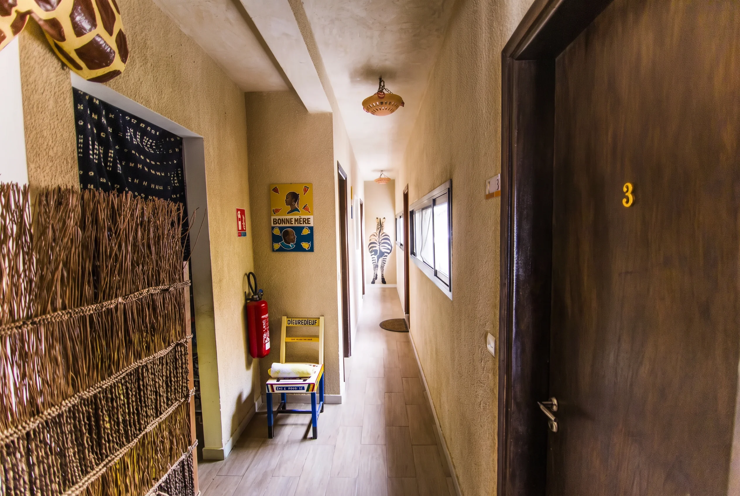 Sand-toned corridor with African art, mudcloth hanging and numbered guest room doors